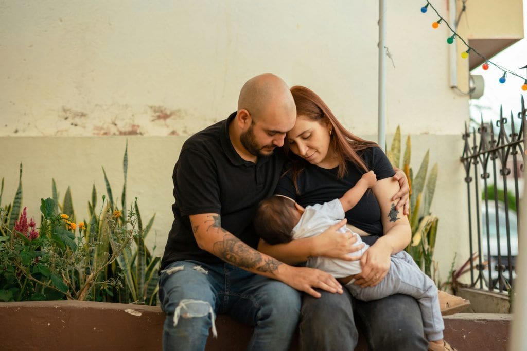 Pareja y posparto: por qué discutimos más y cómo recuperar equipo sin apagar tus necesidades 2 Hombre y mujer sosteniendo en su regazo a su hijo. Terapia perinatal y de pareja online